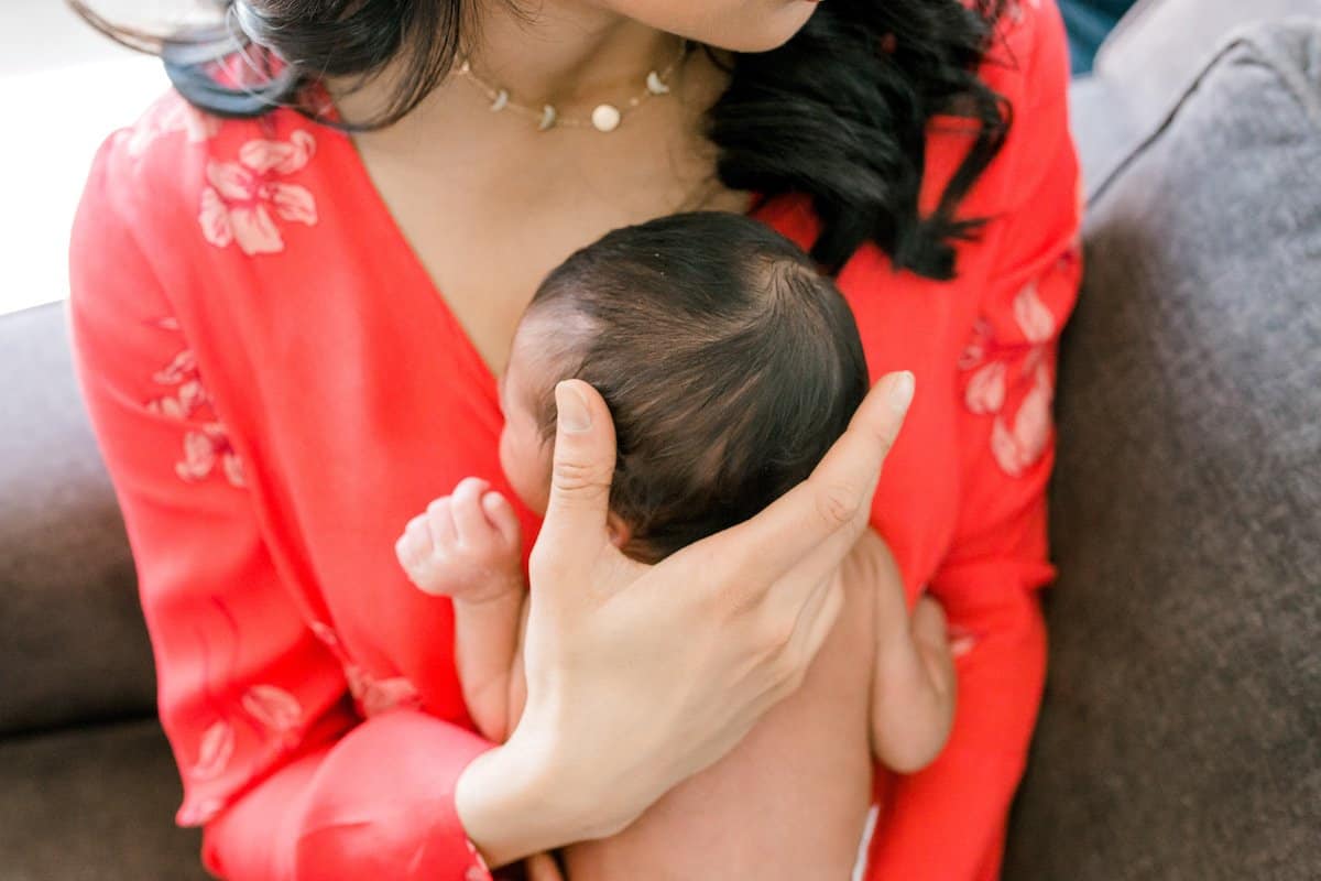 women in coral dress holding a newborn baby to her chest