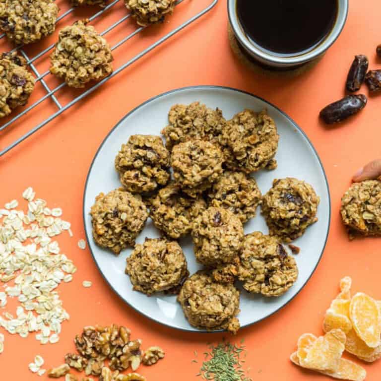 a plate of lactation cookies alongside a cup of coffee and a hand reaching for one cookie.