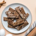 a plate of baby teether biscuits surrounded by cinnamon sticks, a bowl of prunes, eggs, and a rolling pin