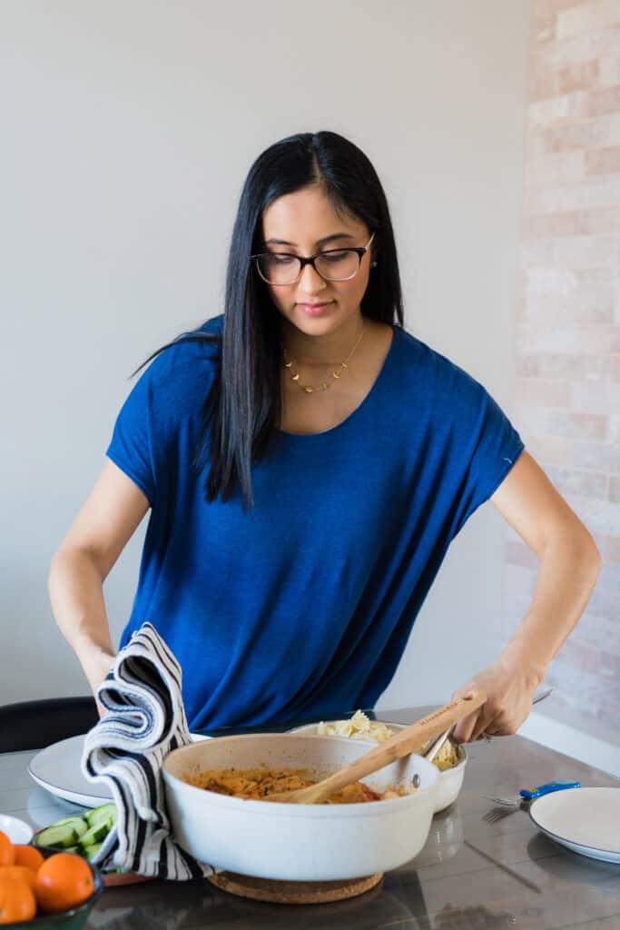 Women with long dark hair and glasses placing dinner on the table.