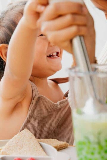 Toddler helping blend up baby food.