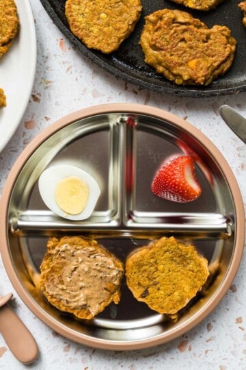 A baby plate with sweet potato fritters spread with a thin layer of almond butter, hardboiled egg, and a strawberry.